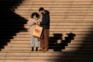 A couple wearing face masks to help protect from the coronavirus check their purchased goods on a staircase at a mall in Beijing, Monday, Jan. 10, 2022. Tianjin, A major Chinese city near Beijing has placed its 14 million residents on partial lockdown after dozens of children and adults tested positive for COVID-19, including at least two with the omicron variant. (AP Photo/Andy Wong)