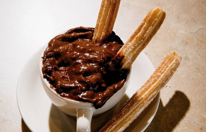Churros covered in sugar beside a thick hot chocolate at La Palma in Miami, Jan. 20, 2022. The combination of churros and hot chocolate has its roots in Spain, but here the union has a distinct Floridian flair. (Scott McIntyre/The New York Times)