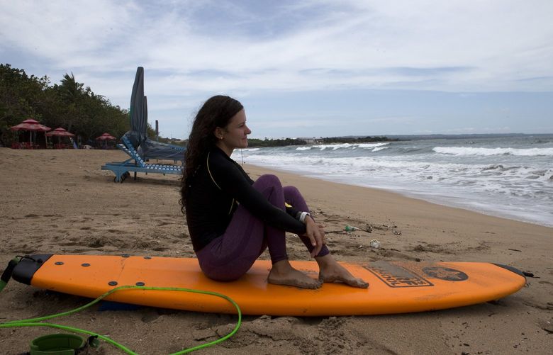 A Russian tourist sits on her surfboard as she watches waves at Kuta beach, Bali, Indonesia on Friday, Feb. 4, 2022. Indonesia is opening the resort island of Bali to foreign travelers from all countries, as international flights resumed for the first time in two years â€” but mandatory quarantines remain in place for all visitors. (AP Photo/Firdia Lisnawati) Bali104 Bali104