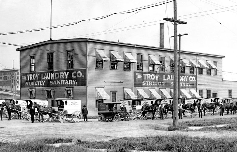 THEN: This northeast-facing 1912 image features 11 horse-drawn and three motor vehicles arranged with their drivers along two sides of Troy Laundry at the northeast corner of Nob Hill and Republican Streets. Drivers, who collected cash receipts, were occasional victims of hold-ups, as reported in the daily papers. Their pay averaged twice that of the “mangle girls.” Credit: Courtesy Ron Edge