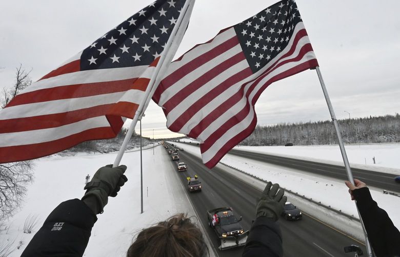 Supporters wave flags at the JBER-Richardson overpass as truckers and other vehicles participate in the Alaska Freedom Convoy 2022 on the Glenn Highway on Sunday, Feb. 6, 2022, to support Canadian truck drivers opposed to COVID-19 vaccine mandates. (Bill Roth/Anchorage Daily News via AP) AKAND201 AKAND201