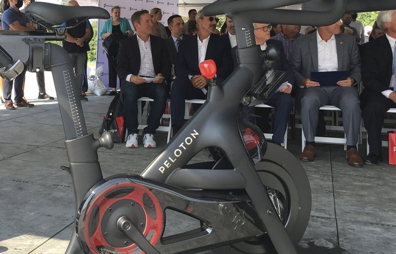 FILE – Peloton CEO John Foley, left, is seen behind one of his company’s fitness machine along with others gathered for the groundbreaking for the company’s first U.S. factory, Monday, Aug. 9, 2021, in Luckey, Ohio.  The co-founder of Peloton is stepping down after an extended streak of tumult at the exercise and treadmill company. John Foley will no longer serve as Peloton’s CEO as of Wednesday, Feb. 8, 2022. Barry McCarthy will take over the role and will also serve as president and a board member.  (AP Photo/John Seewer, File) NYBZ201 NYBZ201