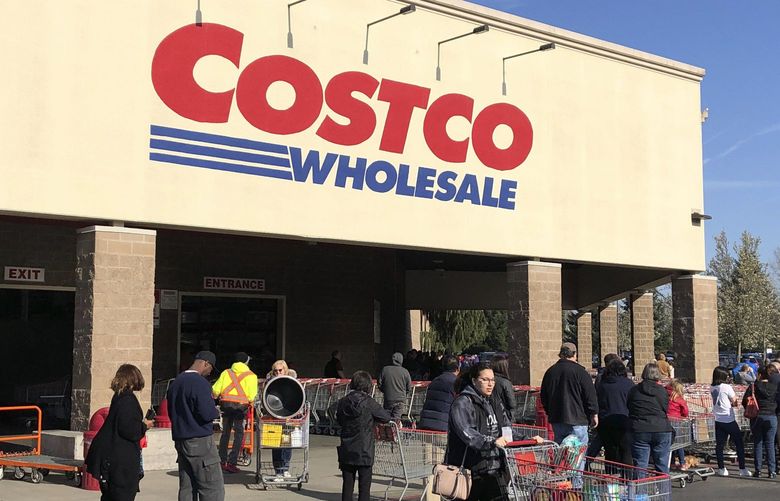 A shopper leaves as others line up to enter a Costco store, Friday, March 20, 2020, in Tacoma, Wash. Consumers continued to stock up on food and other items as officials urged people to stay at home to slow the spread of the new coronavirus. (AP Photo/Ted S. Warren) WATW102