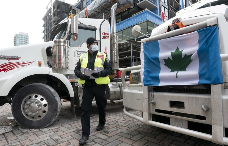 A police officer walks between parked trucks as he distributes a notice to protesters, Wednesday, Feb. 16, 2022 in Ottawa. Ottawaâ€™s police chief was ousted Tuesday amid criticism of his inaction against the trucker protests that have paralyzed Canada’s capital for over two weeks, while the number of blockades maintained by demonstrators at the U.S. border dropped to just one.  (Adrian Wyld /The Canadian Press via AP) ajw116 ajw116