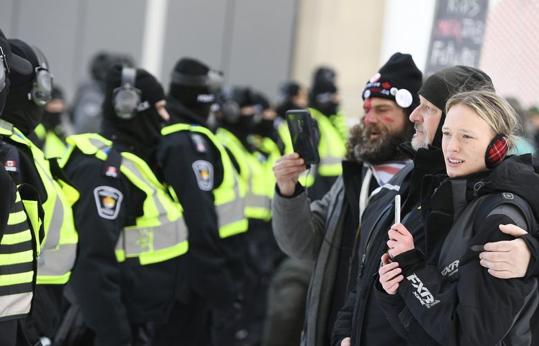 Protesters embrace in front of police officers on Rideau Street near the truck blockade in Ottawa, on Friday, Feb. 18, 2022.  Police began arresting protesters and towing away trucks Friday in a bid to break the three-week, traffic-snarling siege of Canada’s capital by hundreds of truckers angry over the country’s COVID-19 restrictions.(Justin Tang /The Canadian Press via AP) JDT519 JDT519