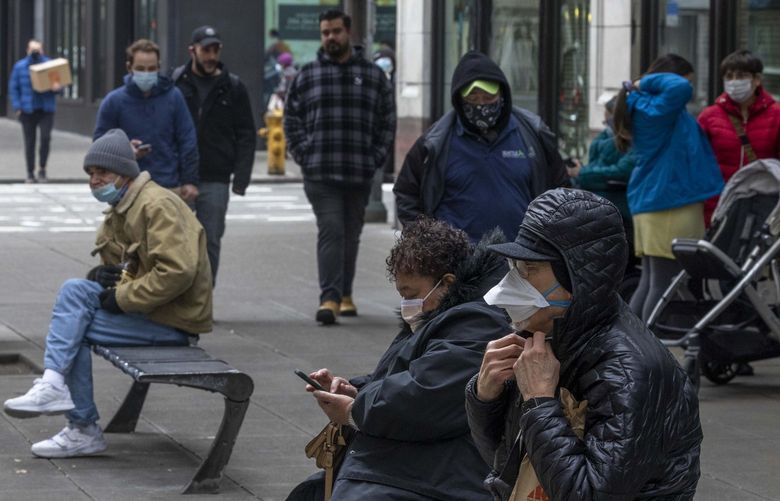 Masked Seattleites wait for buses as pedestrians pass by around noon in downtown Seattle on Feb. 17, 2022. Washington Gov. Jay Inslee announced on Thursday a lift on the mask mandate for schools, businesses to end March 21.