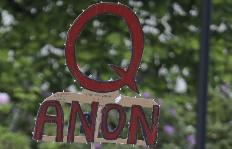FILE – A person carries a sign supporting QAnon during a protest rally in Olympia, Wash., on May 14, 2020. The QAnon conspiracy theory has been linked to acts of real-world violence, including last year’s riot at the U.S. Capitol. In June 2021, a federal intelligence report warned that QAnon adherents could target Democrats and other political opponents for more violence. (AP Photo/Ted S. Warren, File) NYCD801 NYCD801