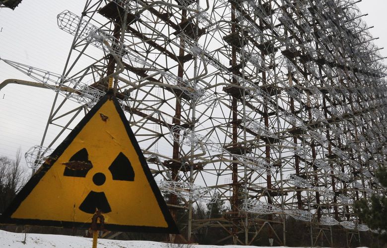 FILE – A Soviet-era top secret object Duga, an over-the-horizon radar system once used as part of the Soviet missile defense early-warning radar network, seen behind a radioactivity sign in Chernobyl, Ukraine, on Nov. 22, 2018. Among the most worrying developments on an already shocking day, as Russia invaded Ukraine on Thursday, was warfare at the Chernobyl nuclear plant, where radioactivity is still leaking from history’s worst nuclear disaster 36 years ago. (AP Photo/Efrem Lukatsky, File) WX153 WX153