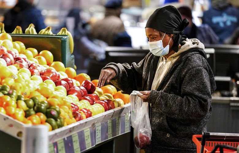 A shopper wearing a protective mask as a precaution against the spread of the coronavirus selects fruit at the Reading Terminal Market in Philadelphia, Wednesday, Feb. 16, 2022. Philadelphia city officials lifted the city’s vaccine mandate for indoor dining and other establishments that serve food and drinks, but an indoor mask mandate remains in place. Philadelphia Public Health officials announced that the vaccine mandate was lifted immediately Wednesday. (AP Photo/Matt Rourke) PAMR102 PAMR102