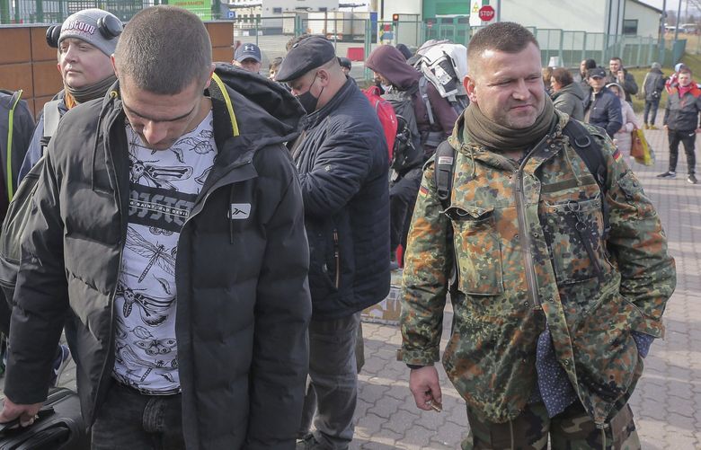 Polish volunteer Jedrzej, 34, in military uniform joins Ukranians, left, waiting to cross the border to go and fight against Russian forces, at Medyka border crossing, in Poland, Saturday, Feb. 26, 2022. (AP Photo/Visar Kryeziu) XVK901 XVK901