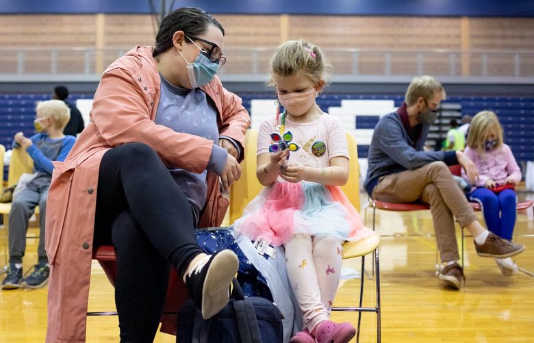 FILE – Fiona Backes, 5, sits with her mother after her first dose of the Pfizer-BioNTech coronavirus vaccine, at a high school gym in Southfield, Mich., Nov. 9, 2021. In a striking reversal, federal regulators said on Feb. 11, 2022 that they would wait for data on whether three doses of Pfizer-BioNTech’s vaccine are effective in children younger than 5 before deciding whether to authorize a vaccine for the age group. (Emily Elconin/The New York Times) XNYT105 XNYT105