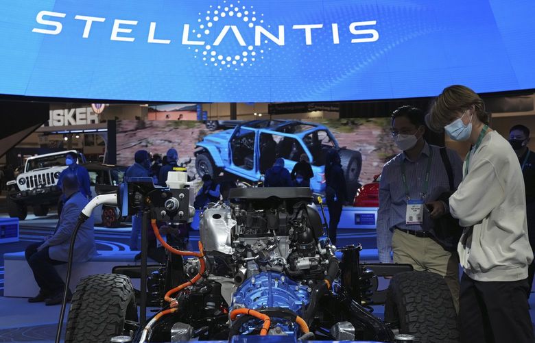 FILE – People look at the charging technology from the Jeep Wrangler 4xe at the Stellantis booth during the CES tech show Thursday, Jan. 6, 2022, in Las Vegas. Automaker Stellantis said Wednesday, Feb. 23, 2022 that it made 13.4 billion euros ($15.2 billion) in its first year after it was formed from the merger of Fiat Chrysler Automobiles and PSA Group.(AP Photo/Joe Buglewicz, File) LBL102 LBL102