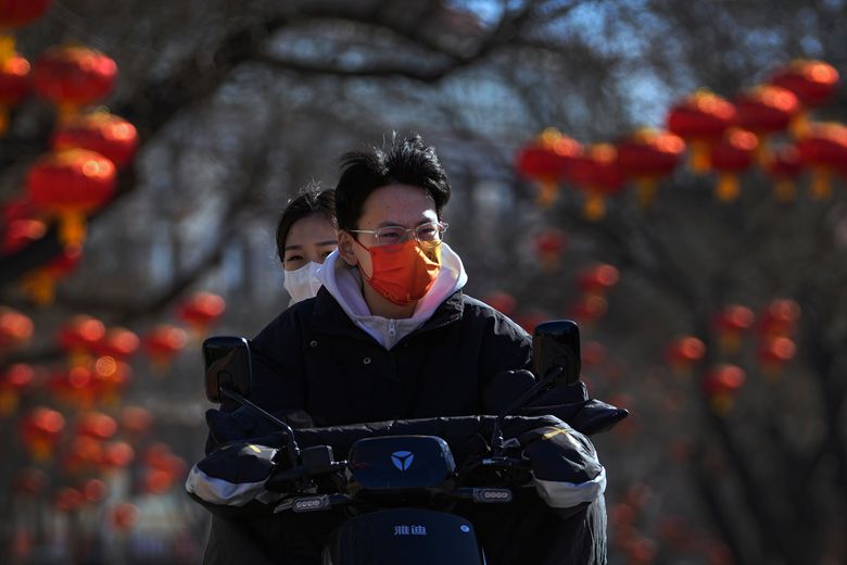 2022 年 2 月 8 日，星期二，北京，戴着口罩以帮助保护免受冠状病毒感染的居民骑着电动滑板车沿着装饰着红灯笼的街道行驶。中国已下令南部城市百色的居民留在家中，并暂停交通联系。 COVID-19 病例的激增至少部分与 omicron 变体有关。 （美联社照片/安迪黄）