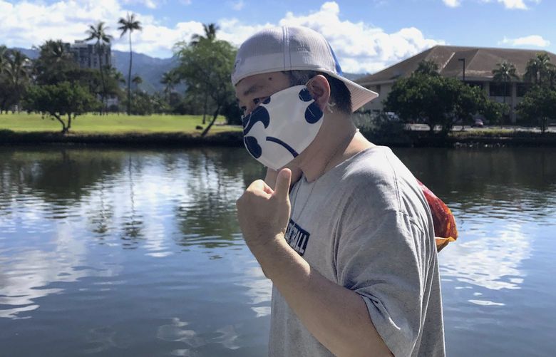 FILE – Ricardo Lay, 52, wearing an aloha print mask, poses for a photo as he walks in the Waikiki neighborhood of Honolulu on April 7, 2020. Hawaii will lift the nation’s last statewide indoor mask mandate by March 26, 2022. Hawaii Gov. David Ige says COVID-19 rates in Hawaii are dropping and he expects the trend to continue in the coming weeks. (AP Photo/Caleb Jones, File) LA206 LA206
