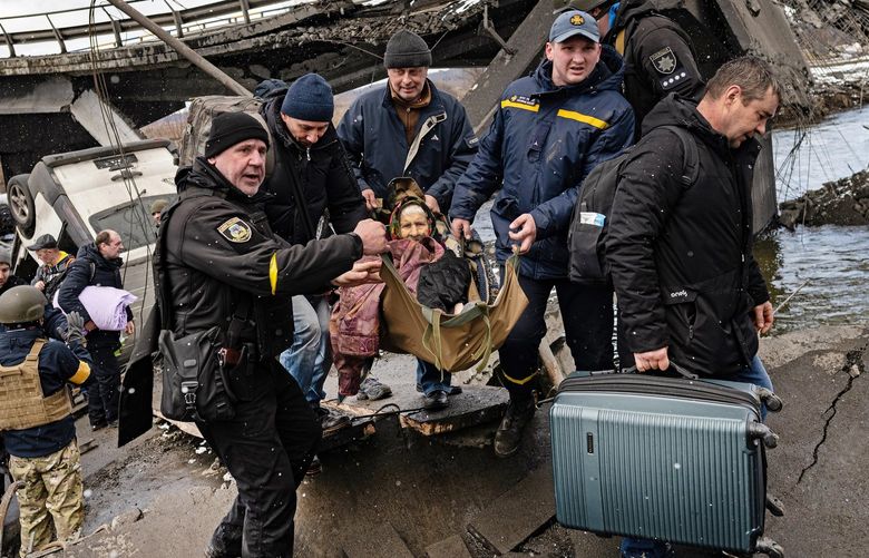 An elderly woman is carried across the Irpin River as civilians flee Irpin, Ukraine on their way to Kyiv on Tuesday, March 8, 2022. About 2,000 civilians were able to escape Irpin, a suburb just northwest of the capital which has spent days without water, power and heat because of the heavy fighting in the area. (Lynsey Addario/The New York Times) – NO SALES – XNYT18 XNYT18