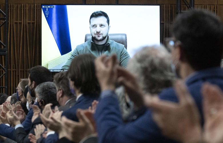 Canadian Members of Parliament and invited guests applaud as Ukrainian President Volodymyr Zelenskyy is shown on a giant video screen before addressing the Canadian parliament, Tuesday, March 15, 2022 in Ottawa.  (Adrian Wyld/The Canadian Press via AP) AJW101 AJW101