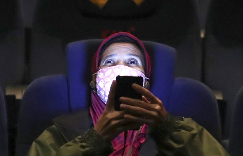A movie theater customer uses her mobile phone before the start of a movie show as she sits amid physical distancing markers during the first day of reopening at a cinema in Jakarta, Indonesia, Thursday, Sept. 16, 2021. (AP Photo/Tatan Syuflana) 