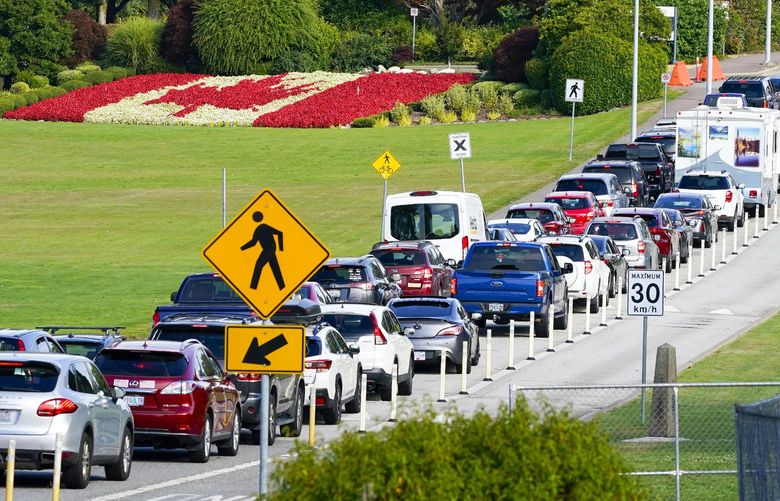 A line of vehicles wait to enter Canada at the Peace Arch border crossing in view of a Canadian flag made of flowers Monday, Aug. 9, 2021, in Blaine, Wash. Canada lifted its prohibition on Americans crossing the border to shop, vacation or visit, but America kept similar restrictions in place, part of a bumpy return to normalcy from coronavirus travel bans. (AP Photo/Elaine Thompson) WAET101