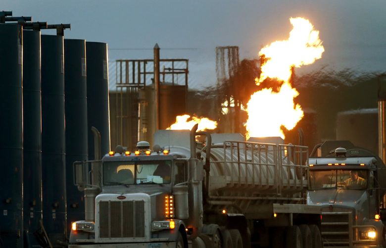 FILE – Drivers and their tanker trucks capable of hauling water and hydraulic fracturing liquid line up near a natural gas burn off flame and storage tanks in Williston, N.D., on June 9, 2014. Under new rules proposed by the Securities and Exchange Commission on Monday, March 21, 2022, companies would be required to disclose the greenhouse gas emissions they produce and how climate risk affects their business, as part of a drive across the government to address climate change. (AP Photo/Charles Rex Arbogast) NY114 NY114