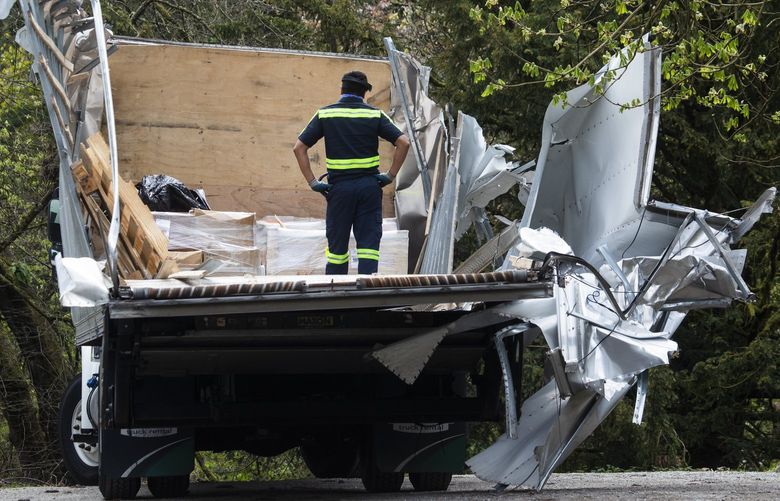 An unidentified man tends to cargo in the back of a box truck that had its top sheared off under the Arboretum Aqueduct pedestrian bridge, Tuesday, March 29, 2022 in Seattle’s Washington Park Arboretum. The bridge, which is well marked with signs warning about height limits, did not appear damaged. 219994