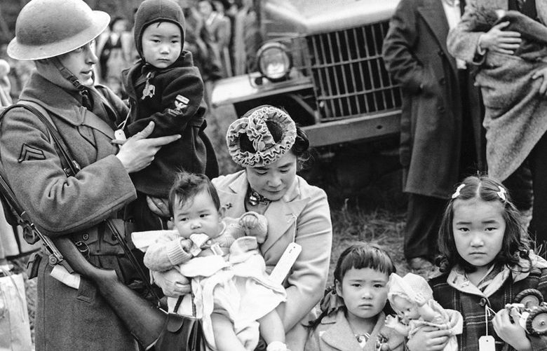 Mrs. Shigeho Kitamoto had no time for tears when she was evacuated along with other Japanese from Bainbridge Island in Washington State, March 30, 1942. She has too busy looking after her four children.  Corporal George Bushy, member of the military guard which supervised the departure of 237 Japanese for California, gave her a hand with the youngest.  (AP Photo)