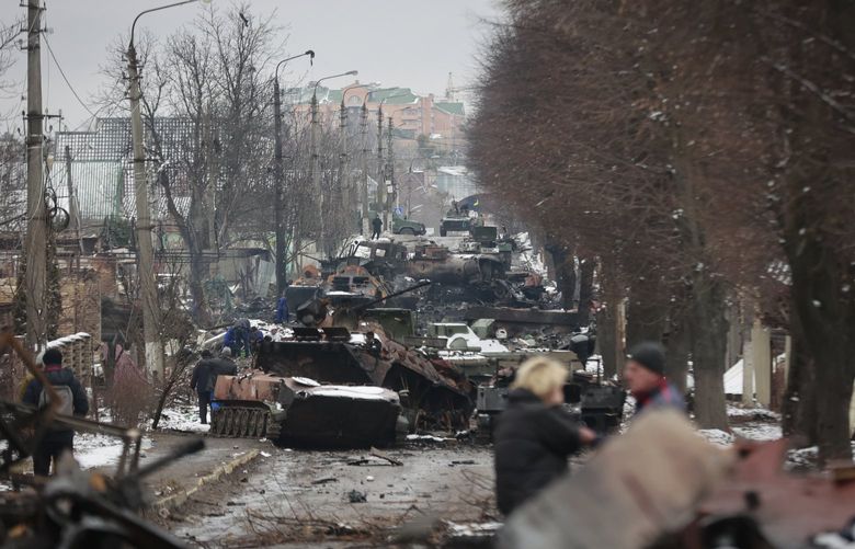 People look at the gutted remains of Russian military vehicles on a road in the town of Bucha, close to the capital Kyiv, Ukraine, Tuesday, March 1, 2022. (AP Photo/Serhii Nuzhnenko) NYAG814 NYAG814