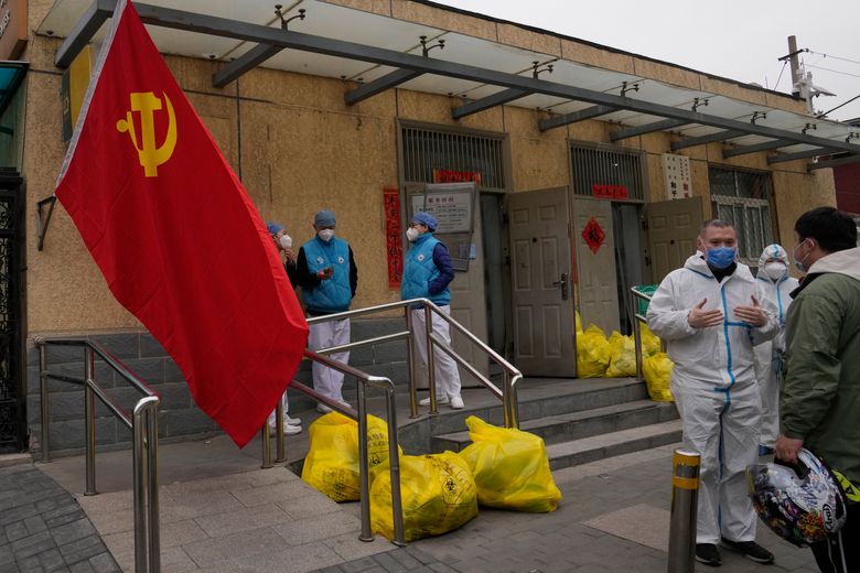 2022 年 3 月 17 日星期四，北京，一个封闭的社区外的社区工作人员在共产党旗帜和标有危险废物的垃圾袋旁聊天。 即使当局在中国爆发两年来最严重的疫情中封锁了城市，他们仍在寻找成功但繁重的 COVID-19 预防策略的出口坡道。 （美联社照片/吴汉冠）