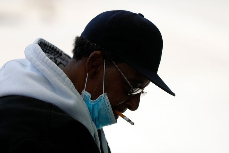 文件——2020 年 4 月 8 日，星期三，一名戴着防护面具的男子在底特律等公共汽车时抽着烟。美国的吸烟率在 2020 年降至历史新低，八分之一的成年人表示他们目前是吸烟者，根据疾病控制和预防中心于 2022 年 3 月 17 日星期四发布的调查数据。 CDC 报告称，成人电子烟的使用量也有所下降。 （美联社照片/Paul Sancya，档案）