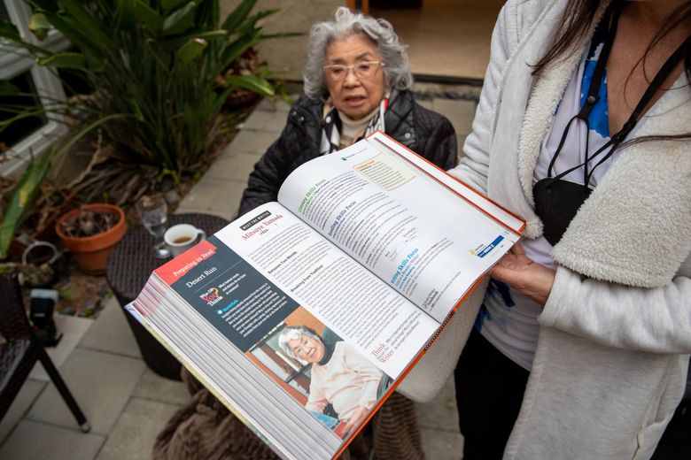 Hedi Mouchard, Mitsuye Yamada’s daughter, holds up a text book that her own daughter, Alana, had in high school that had a small section about her grandmother from their home, Feb. 21, 2022 in Irvine, Calif. (Jennifer Buchanan / The Seattle Times)