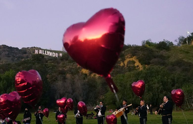 FILE – A Mexican Mariachi band surrounded by heart-shaped balloons awaits the arrival of a couple’s wedding proposal ceremony at the Lake Hollywood Park in Los Angeles, on Valentine’s Day, Feb. 14, 2022. Attending weddings can be expensive, between travel and lodging, gifts and extra events like bachelor and bachelorette parties. So plan ahead for these expenses, particularly as wedding season approaches and celebrations that were postponed or rescheduled reappear on your calendar.   (AP Photo/Damian Dovarganes, File) 