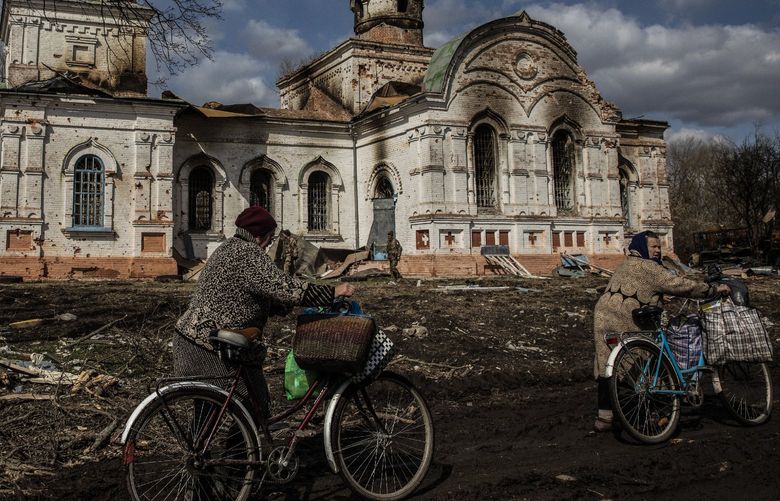 A woman rides bicycles past the damaged Voznesenska Church, built in 1913, in Lukashivka, Ukraine, on April 4, 2022. MUST CREDIT: Photo for The Washingto Post by Heidi Levine