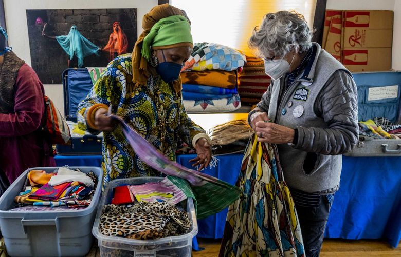 Afua Wokomaokereke, center shows Merlin Rainwater, right, a skirt at the market place at Wa Na Wari in the Central District in Seattle on Saturday April 2, 2022.