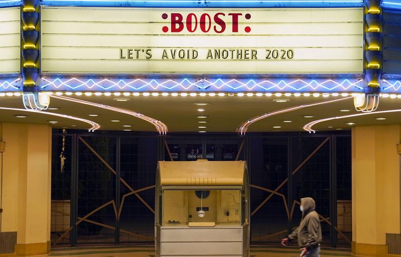 A man walks underneath the marquee of the Alex Theatre in Glendale, Calif., which bears a message urging people to get COVID-19 vaccine booster shots, Monday, Jan. 24, 2022. (AP Photo/Chris Pizzello) CACP101