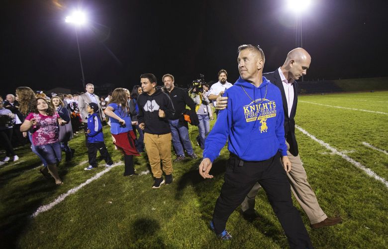 FILE – Bremerton High assistant football coach Joe Kennedy, front, walks off the field with his lawyer, right, Oct. 16, 2015, after praying at the 50-yard line following a football game in Bremerton, Wash. After losing his coaching job for refusing to stop kneeling in prayer with players and spectators on the field immediately after football games, Kennedy will take his arguments before the U.S. Supreme Court on Monday, April 25, 2022, saying the Bremerton School District violated his First Amendment rights by refusing to let him continue praying at midfield after games. (Lindsey Wasson/The Seattle Times via AP, File) WASET501 WASET501