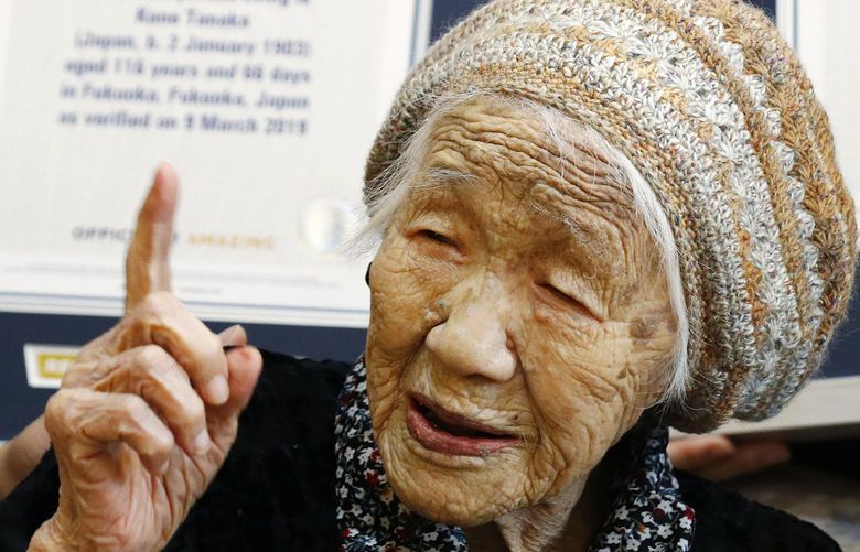 FILE – Kane Tanaka, then 116-years-old, reacts after receiving a Guinness World Records certificate, background, at a nursing home where she lives in Fukuoka, southwestern Japan on March 9, 2019. The Japanese woman recognized as the world’s oldest person Tanaka has died at age 119, just months short of her goal of reaching 120. (Takuto Kaneko/Kyodo News via AP, File) TKMY101 TKMY101