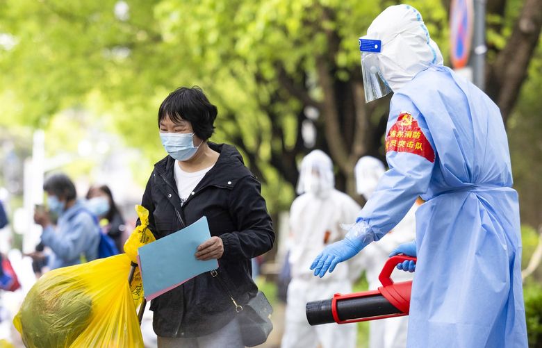In this photo released by Xinhua News Agency, a villager carrying baggage is disinfected as she returns home after being quarantined due to local COVID cases found in Lianqin Village of Beicai Town in Pudong New Area, Shanghai on Tuesday, April 26, 2022. Shanghai city authorities said Wednesday they will start rounds of COVID-19 testing over the next few days to determine which neighborhoods can safely be allowed a limited amount of freedom of movement, as residents in Beijing watch carefully on word for whether the capital city will lock down. (Jin Liwang/Xinhua via AP) XIN805