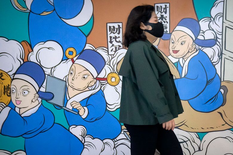 2022 年 4 月 22 日，星期五，一名戴着口罩的妇女走过北京的一幅壁画。上海官员周五承诺，在试图重振当地经济的同时，将放松对阻碍食品供应和贸易的卡车司机的防病毒控制。数百万人仍被限制在家中。 （美联社照片/马克 Schiefelbein）
