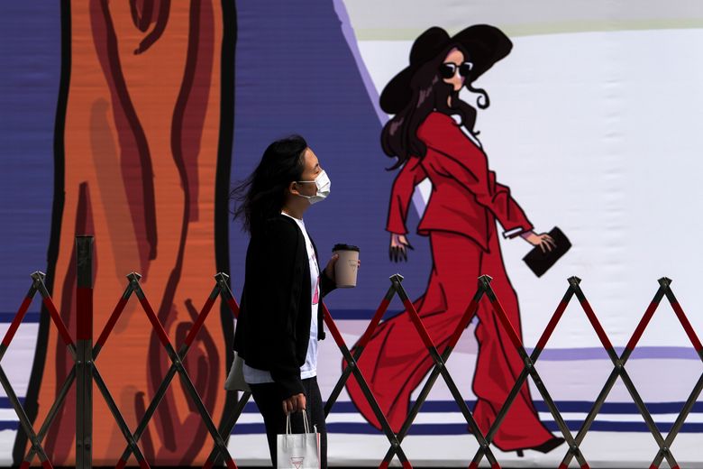 一名戴着口罩以帮助保护免受冠状病毒感染的妇女走过一堵展示时尚卡通画的街垒建筑墙。 在 10 名中学生的 COVID-19 检测呈阳性后，北京处于戒备状态，该市官员称这是第一轮检测。 （美联社照片/安迪黄）