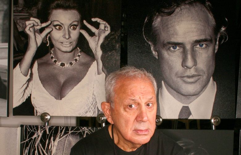 FILE â€” Ron Galella and a few of his celebrity photos at his home in Montville, N.J., Sept. 15, 2006. Galella, the freelance photographer who relentlessly pursued Jacqueline Kennedy Onassis until a judge barred him from taking her picture, who pestered Marlon Brando until Brando broke his jaw, and who helped define todayâ€™s boundary-challenged culture of celebrity, died on Saturday, April 30, 2022, at his home in Montville, N.J. He was 91. (Fred R. Conrad/The New York Times) XNYT262