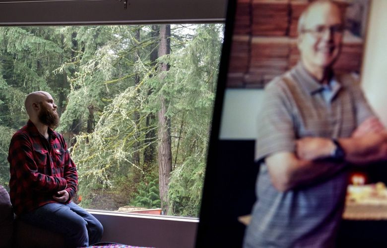 Nathan Lambrecht is photographed next to a picture of his father, Doug Lambrecht, at his apartment in Woodinville, Wash., Monday, March 21, 2022. The 71-year-old retired physician was among the first of the nearly 1 million Americans to die from COVID-19. “I’m afraid that as the numbers get bigger, people are going to care less and less,” Nathan said. “I just hope people who didn’t know them and didn’t have the same sort of loss in their lives due to COVID, I just hope that they don’t forget and they remember to care.” (AP Photo/David Goldman) WADG201 WADG201