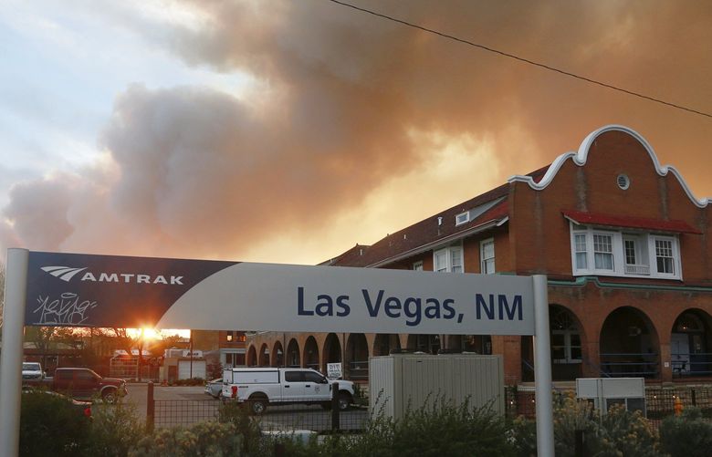 A sunset seen through a wall of wildfire smoke from the Amtrak train station in Las Vegas, N.M., on Saturday, May 7, 2022. The CastaÃ±eda Hotel, right, hosted meals for residents and firefighters this week with sponsorships from restaurants and other businesses. (AP Photo/Cedar Attanasio) NMCA704 NMCA704