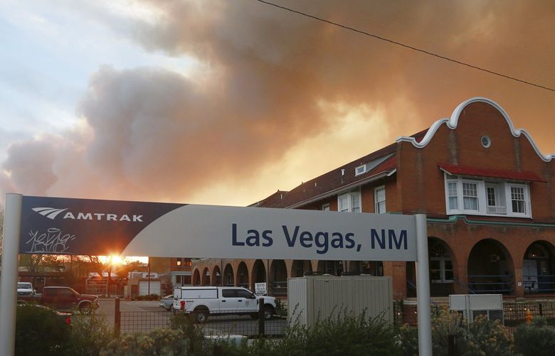 A sunset seen through a wall of wildfire smoke from the Amtrak train station in Las Vegas, N.M., on Saturday, May 7, 2022. The Castañeda Hotel, right, hosted meals for residents and firefighters this week with sponsorships from restaurants and other businesses. (AP Photo/Cedar Attanasio) NMCA704 NMCA704