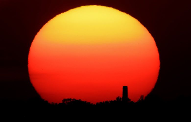 FILE – In this Friday, June 26, 2020 file photo, the sun sets behind a smokestack in the distance in Kansas City, Mo. According to a World Meteorological Organization forecast for the next five years, released on Thursday, May 27, 2021, it’ll likely be so hot that there’s a 40% chance in the next few years that the globe will push past the temperature limit set by the Paris climate agreement. (AP Photo/Charlie Riedel, File)