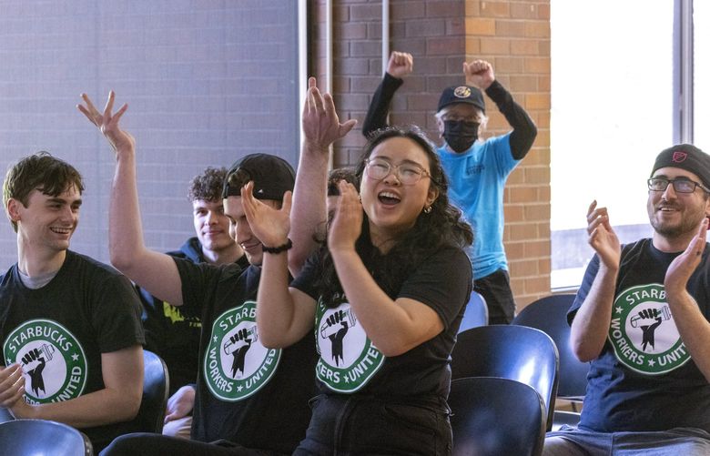 Emily Sirisue jumps up to show her support with other Seattle Starbucks baristas after the vote comes in to unionize the Starbucks roastery on Capitol Hill. Workers gathered at Seattle Central College Thursday, April 21, 2022, to watch the vote count on a zoom call, projected on a screen at the front of the room. L – R: William Cavanagh (who is the only one who does not work at the roastery), Brennen Collins, Sirisue and Zach Simon. All are Starbucks baristas. 104 employees were eligible to vote, 69 did, one vote was void, three were challenged and the final vote was 38-27 in favor of joining the union. 220191