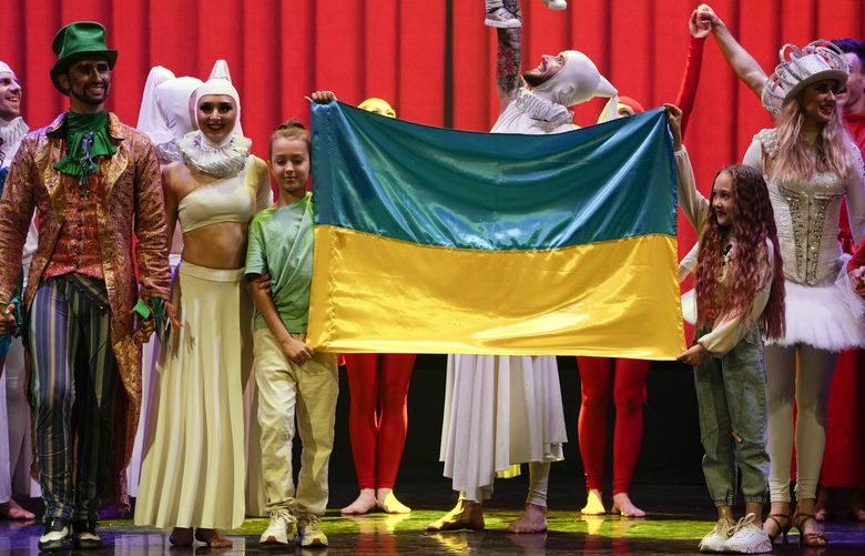 Performers stand on stage with the Ukrainian flag, held by two of their children, and baby Milena hoisted up above it at the end of the show “Alice in Wonderland” in Pistoia, Italy, Friday, May 6, 2022. A Ukrainian circus troupe is performing a never-ending â€œAlice in Wonderlandâ€ tour of Italy. They are caught in the real-world rabbit hole of having to create joyful performances on stage while their families at home are living through war. The tour of the Theatre Circus Elysium of Kyiv was originally scheduled to end in mid-March. (AP Photo/Alessandra Tarantino) ALT124 ALT124