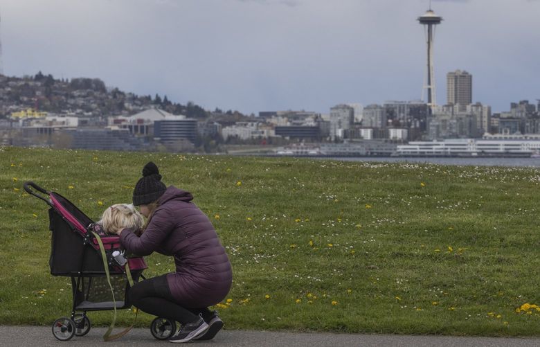 Under cloudy but rainless skies, a woman pauses during a walk to chat with her dog while taking a walk along the waterfront in West Seattle Monday, April 11, 2022.  Rain is predicted for Tuesday but the rest of the week should be sunny.

 220095