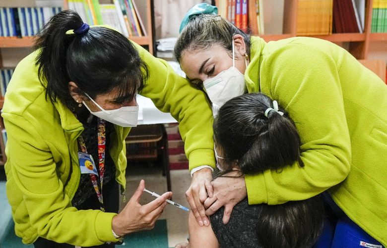 Healthcare workers give a child a booster shot of the pediatric Pfizer COVID-19 vaccine at Paul Harris School in Santiago, Chile, Friday, May 13, 2022. (AP Photo/Esteban Felix) EFX103