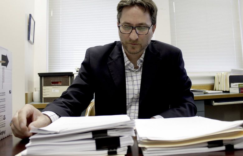 FILE – Carl Macpherson, executive director at Metropolitan Public Defender, examines the file in a double murder case that was recently pushed back for trial in his office in Portland, Ore., on May 5, 2022. (AP Photo/Gillian Flaccus, File) FX703 FX703