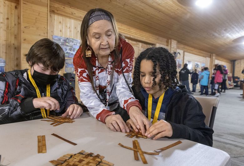 Grace Hyasman, a canoe journey specialist with the Nisqually Tribe, helps Christian Jensen weave a mat during a workshop at the Nisqually Cultural Center in DuPont, Pierce County, last month. At left is Jordan James. They and other fourth graders from Meadows Elementary School visited the center as part of a North Shore Public Schools curriculum to teach students about Native history, traditions and culture. (Ellen M. Banner / The Seattle Times)