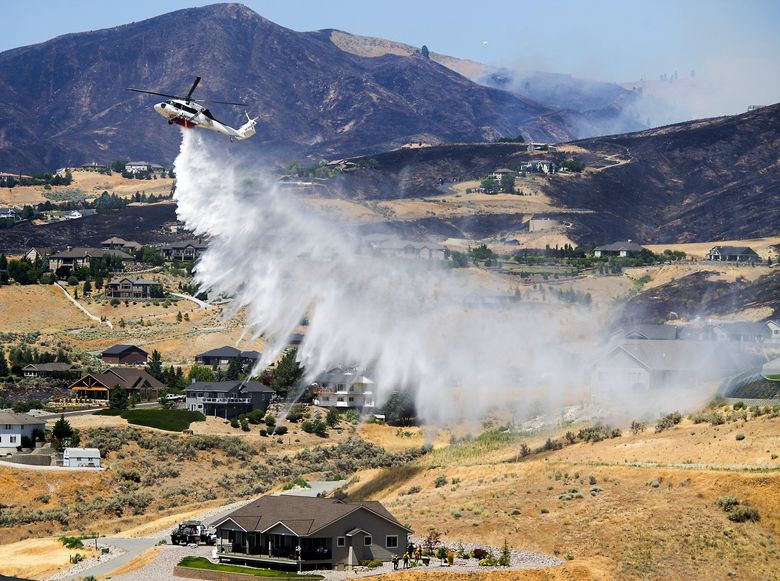 A helicopter makes a drop over houses along Sky Crest Lane in Wenatchee before firefighters begin a burnout at the Red Apple Fire on July 14, 2021. (Don Seabrook / The Wenatchee World)